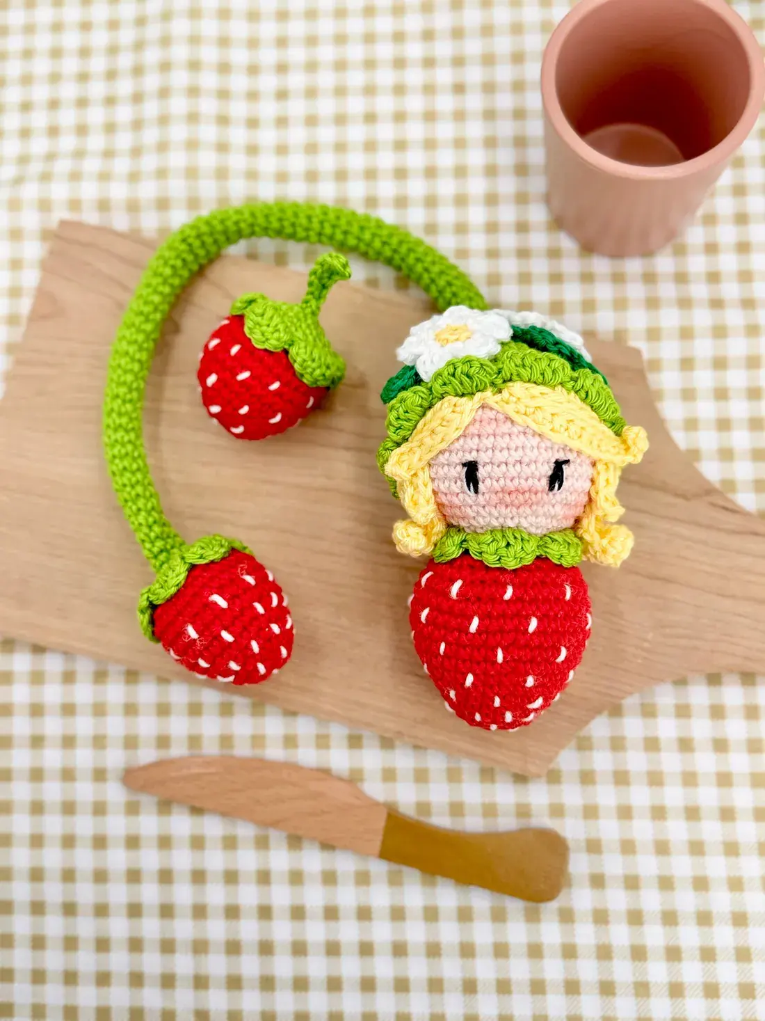 Poupée fraise des Croch’fruits sur une planche en bois, avec ses fraises